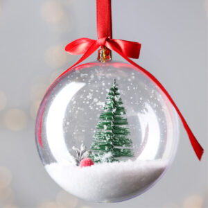 Eine durchsichtige Christbaumkugel mit einem Christbaum und Schnee drinnen.