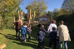 Eine Gruppe von Kindern und drei Erwachsene gehen gemeinsam auf einen neu gestalteten Kletter- und Spielbereich aus Holz zu. Der Bereich ist mit bunten Luftballons, einem Absperrband und einem großen ‚DANKE‘-Plakat geschmückt.