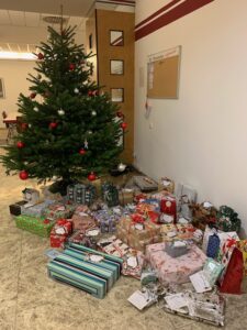 Ein geschmückter Weihnachtsbaum steht in einer Filiale der Stadtsparkasse Augsburg. Darunter und davor liegen zahlreiche bunt verpackte Weihnachtsgeschenke, die im Rahmen einer Geschenkaktion gesammelt wurden.