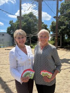 Cornelia Kollmer, stellvertretende Vorstandsvorsitzende der Stadtsparkasse Augsburg, übergibt Sigrun Maxzin-Weigel vom Evangelischen Kinder- und Jugendhilfezentrum Augsburg 50 Freikarten für den Zoo Augsburg. Beide stehen lächelnd vor einem Kletterparcours und präsentieren die Eintrittskarten.