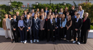 Gruppenfoto der neuen Auszubildenden der Stadtsparkasse Augsburg. Rund 30 junge Menschen und Mitarbeitende stehen gemeinsam vor einer begrünten Außenwand und blicken in die Kamera.